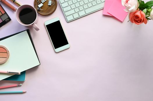 Top view image of woman accessories putting on the pink working desk, including keyboard, coffee cup, bouquet, notebook, pen, mobile, cosmetics and paper clip. Feminine working desk concept.