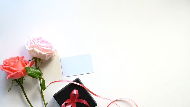 Top view copy space of pink and white rose close to black present box with red ribbon all of these putting on the white table as background. Surprising Valentines Day gift concept.