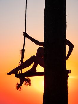 Young woman on a swing at the beach at sunset