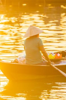 Vietnamese woman in traditional bamboo hat rowing on the Thu Bon River in evening