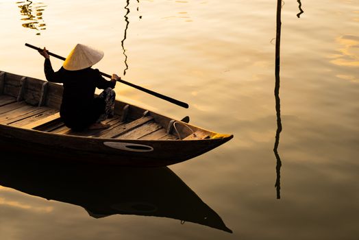 Vietnamese woman in traditional bamboo hat rowing on the Thu Bon River in evening