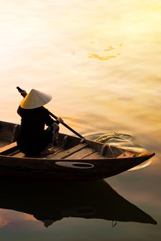 Vietnamese woman in traditional bamboo hat rowing on the Thu Bon River in evening