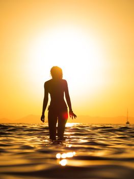 Silhouette of a young woman walking in the sea at sunset