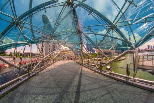 Singapore - APRIL 20 2018: Scenic view of the Helix Bridge. The Marina Bay Sands Hotel with the SkyPark on the top of towers is visible on blue sky background. Wonderful cityscape.