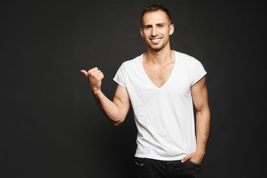 A smiling male fitness model with sporty perfect body points finger to the right. Advertising sports goods and services.
