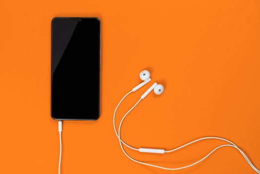 Close-up of smart phone with Earphones on a Orange background. (Top view). Listen to music.