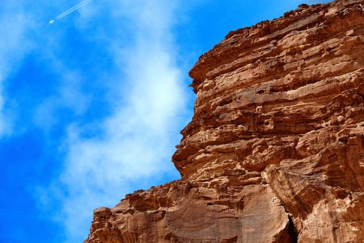 Cut monolith in the desert of the nature reserve of Wadi Rum, in the sky with an airplane that generates contrails, Jordan, midde east