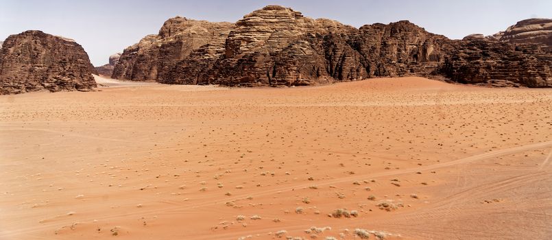 The emptiness of the great desert in the nature reserve of Wadi Rum, with large mountains of red sandstone in the background and the view over the wide sandy plain, Jordan