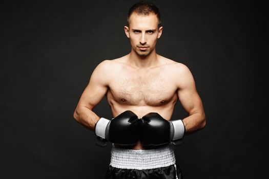 A young male boxer with athletic perfect body in boxing gloves isolated at dark background. Advertising sports goods and services.