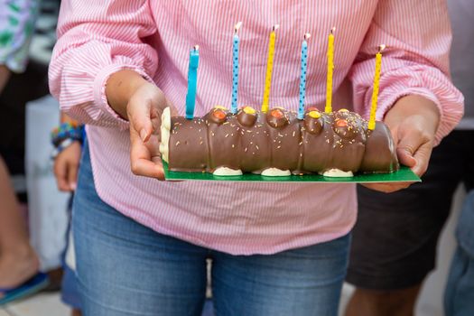 A woman carrying a chocolate log birthday cake with five lit candles