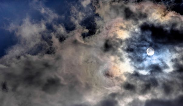 Dramatic sky with some dark and many white clouds covering the sun and making it semi-transparent, abstract or background