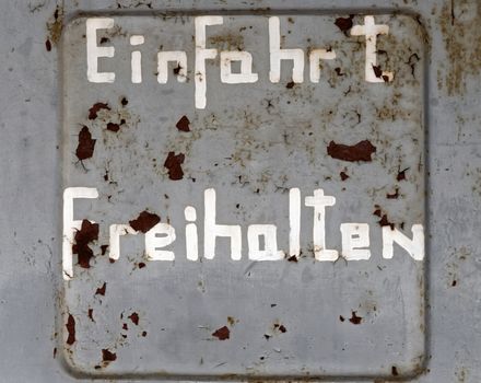 Flaking old weathered German inscription "Keep entrance free", on an ugly grey wall with too little paint and spots of rust, concept