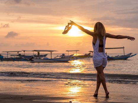 Woman on the beach in Bali Indonesia holding her sandals at sunset