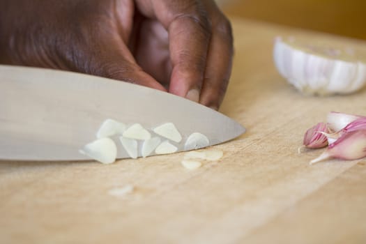 A black man chopping garlic on a woden chooping board