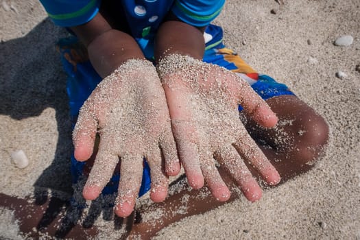 Young boy with sandy hands sat on the beach