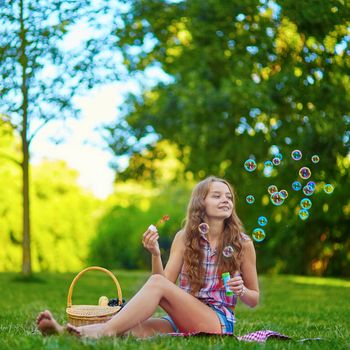Young girl sitting on the grass and blowing bubbles on a summer day