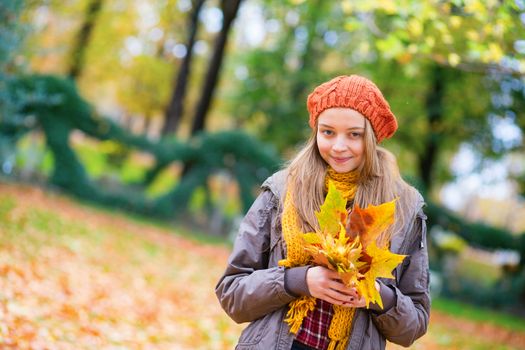 Cheerful young girl with bunch of leaves on a fall day