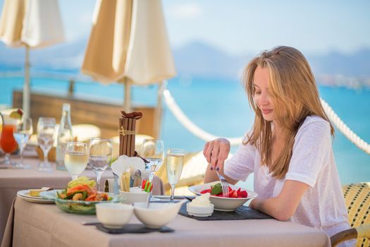 Beautiful young woman eating fruits in a beach restaurant