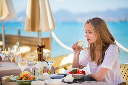 Beautiful young woman drinking champagne in a beach restaurant