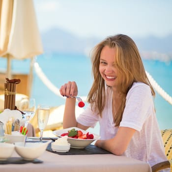 Beautiful young woman eating fruits in a beach restaurant