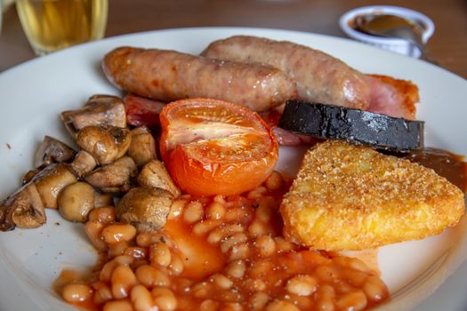 Traditional English breakfast with sausage, bacon, mushrooms, hash browns, tomato, black pudding but no egg