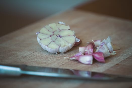 Raw garlic (Allium sativum) being chopped on a wooden chopping board