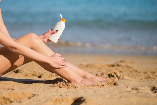 Beautiful young woman applying sunscreen on her legs