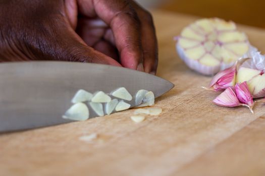 Black person chopping raw garlic (Allium sativum) on a wooden chopping board