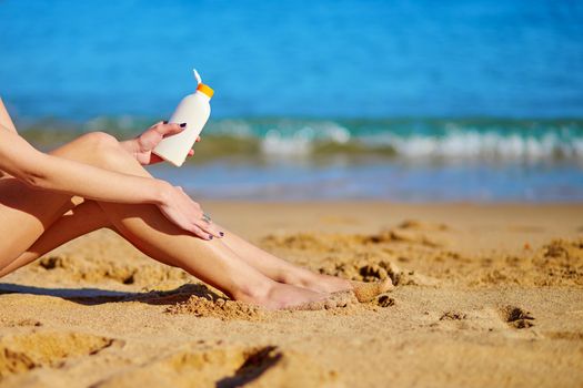 Beautiful young woman applying sunscreen on her legs