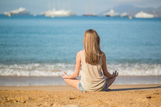 Beautiful young woman meditating on the beach