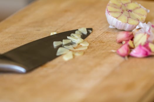 Raw garlic (Allium sativum) being chopped on a wooden chopping board