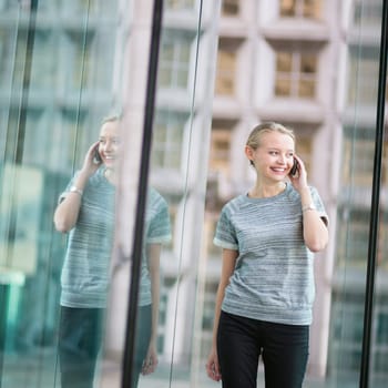 Young beautiful business woman in modern glass interior speaking on the phone