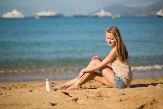 Beautiful young woman applying sunscreen on her legs