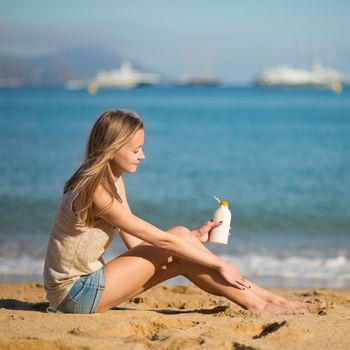 Beautiful young woman applying sunscreen on her legs