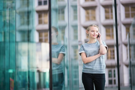 Young beautiful business woman in modern glass interior speaking on the phone