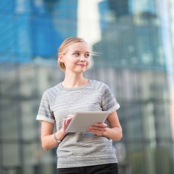 Smiling young woman in modern glass office interior using tablet