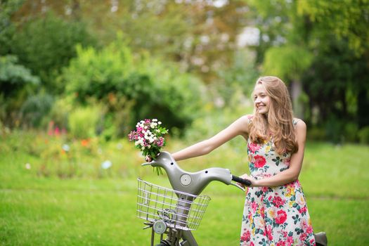 Happy young girl with bicycle in park on a summer day