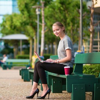 Young beautiful business woman drinking coffee and working on her laptop outdoors