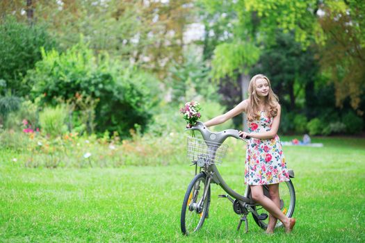 Happy young girl with bicycle and flowers in countryside on a summer day
