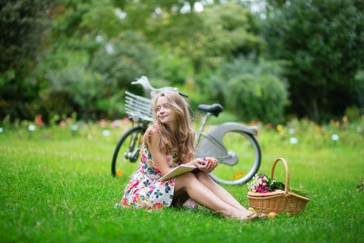 Young girl sitting on the grass and reading a book in the countryside 