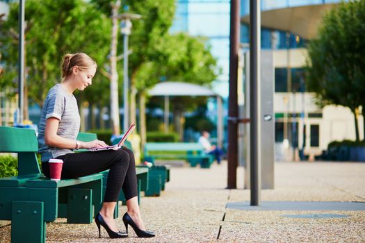Young beautiful business woman or student drinking coffee and working on her laptop outdoors