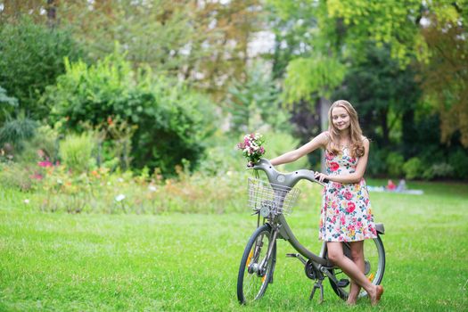 Happy young girl with bicycle and flowers in countryside on a summer day 