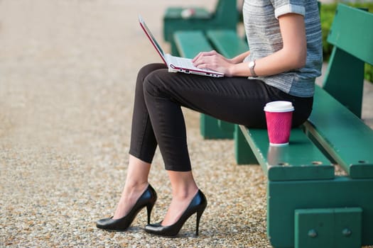 Young beautiful business woman drinking coffee and working on her laptop outdoors