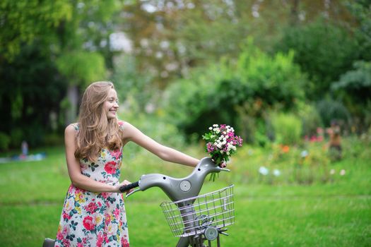Happy young girl with bicycle and flowers in countryside on a summer day 