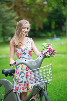 Happy young girl with bicycle and flowers in countryside on a summer day 