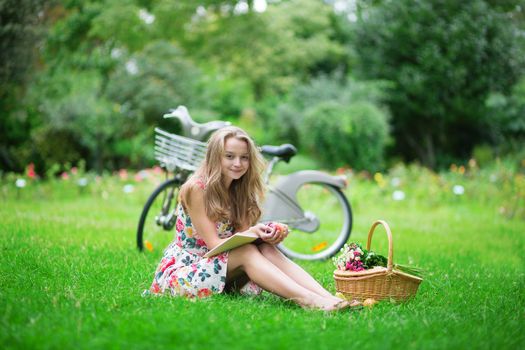 Beautiful young girl with bicycle in the countryside, reading a book