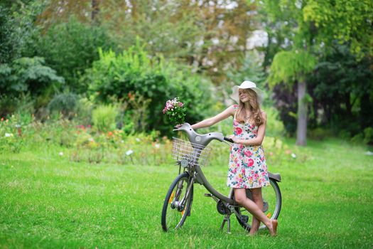 Happy young girl with bicycle and flowers in countryside on a summer day