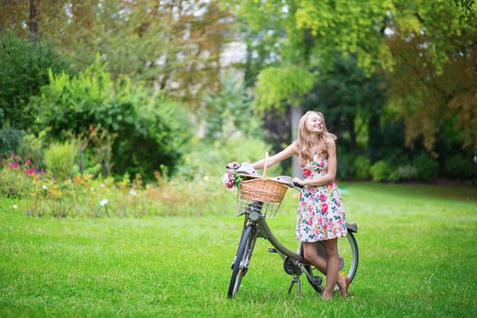 Happy young girl with bicycle and flowers in countryside on a summer day