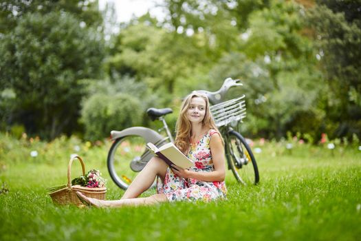 Beautiful young girl with bicycle in the countryside, reading a book