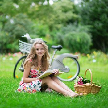 Beautiful young girl with bicycle in the countryside, reading a book